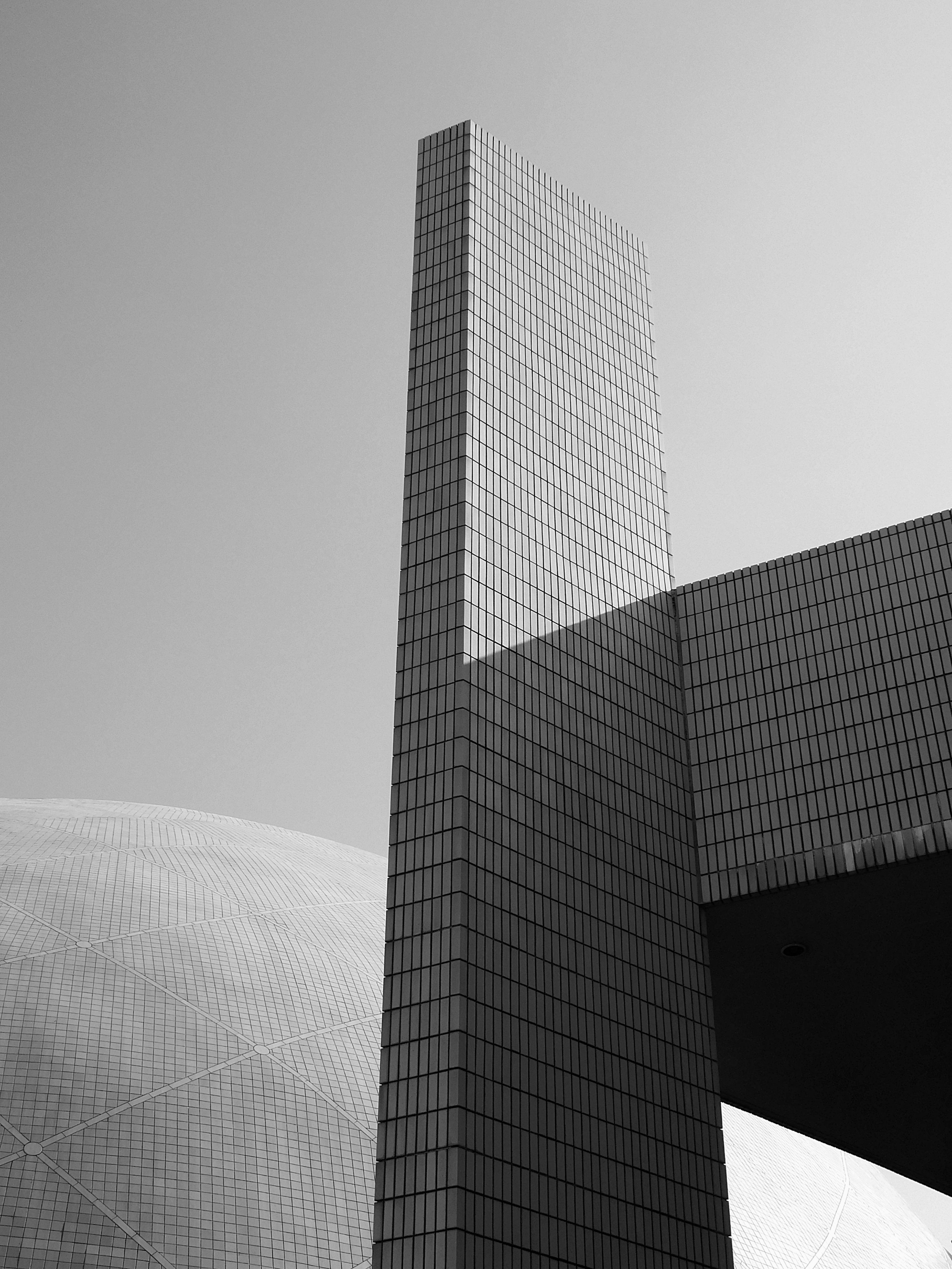 Free Low angle black and white of contemporary high geometric exterior of glass skyscraper in daytime under sky Stock Photo