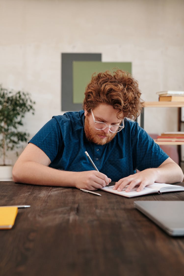 Man In Blue Shirt Writing On A Notebook