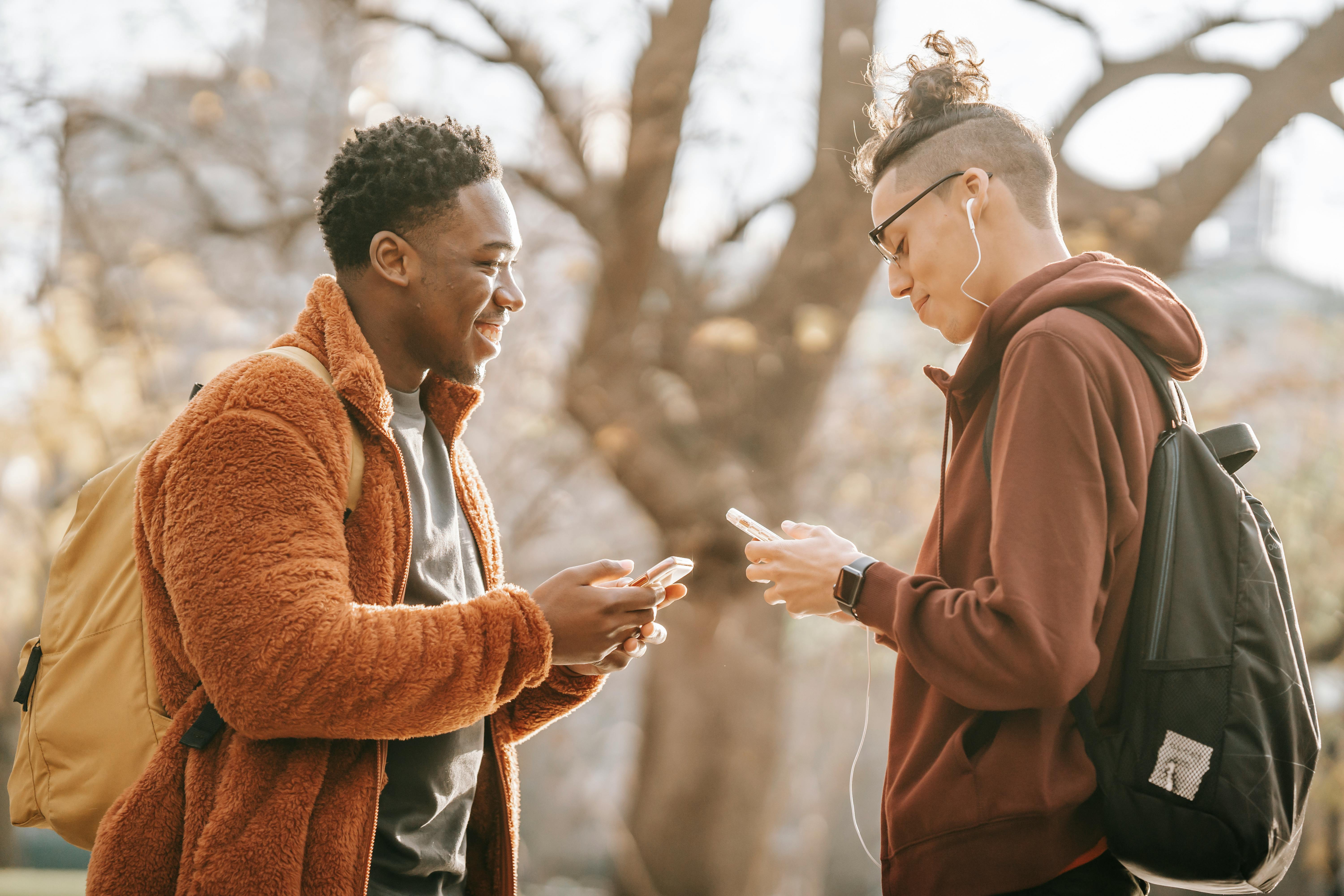 smiling diverse male guys browsing modern cellphones against blurred trees