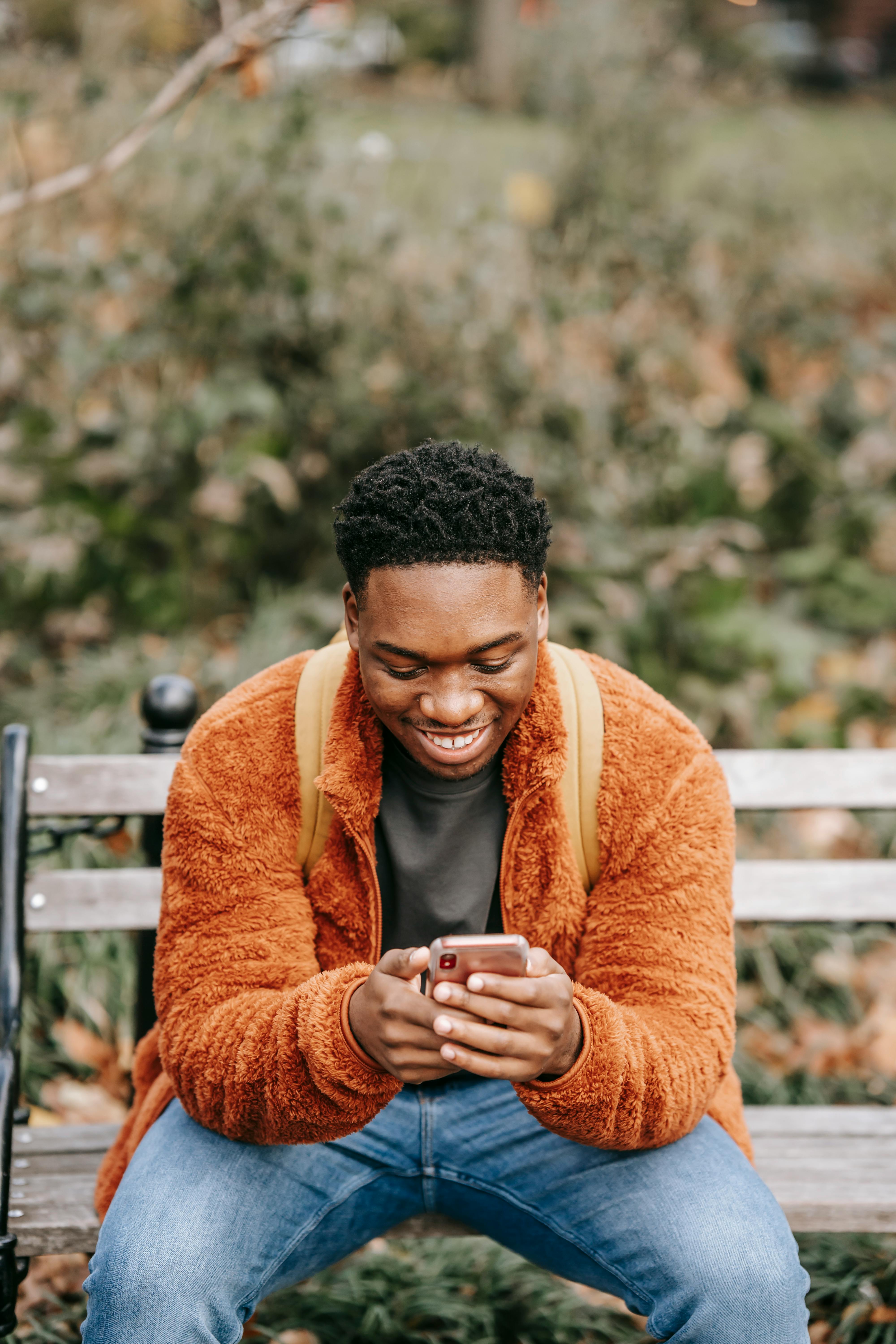 young black man smiling while using smartphone in city park