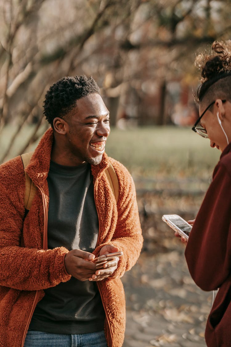 Positive Young Male Friends Using Modern Smartphones In Park