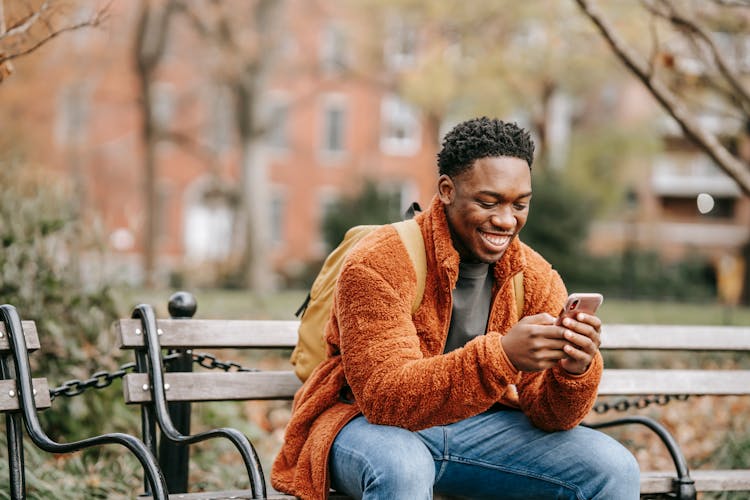 Delightful African American Man Surfing Modern Cellphone In City Park