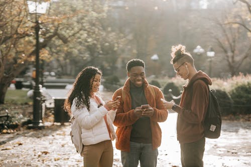 Multiracial positive male and female students using smartphones in city park