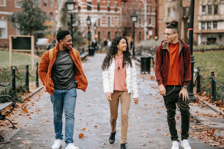 Positive Young Ethnic Guys With Female Friend Walking Along Pathway In City