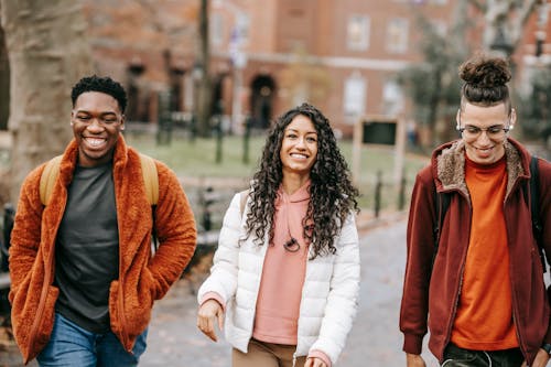 Free Happy multiracial friends in trendy outfits smiling while strolling together in city park Stock Photo