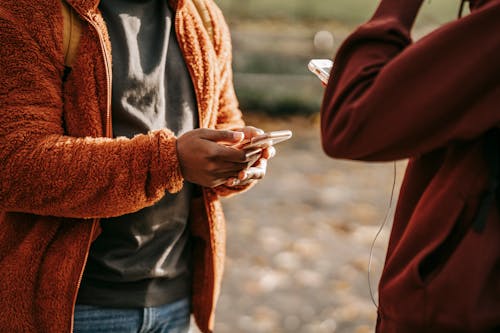 Crop friends browsing smartphones on street