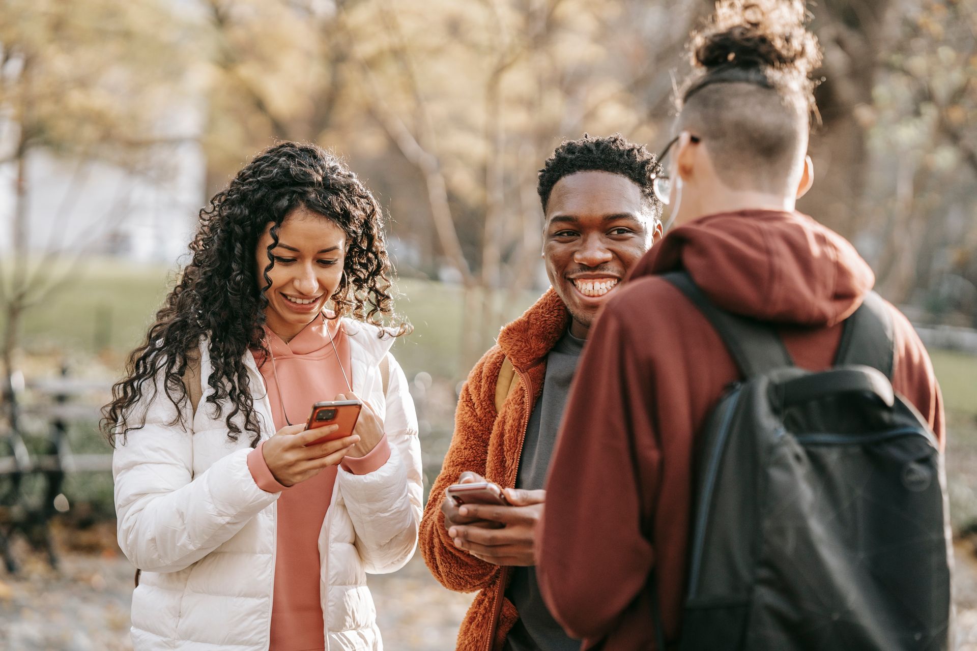 A cheerful group of friends enjoying a conversation and using smartphones outside during fall.