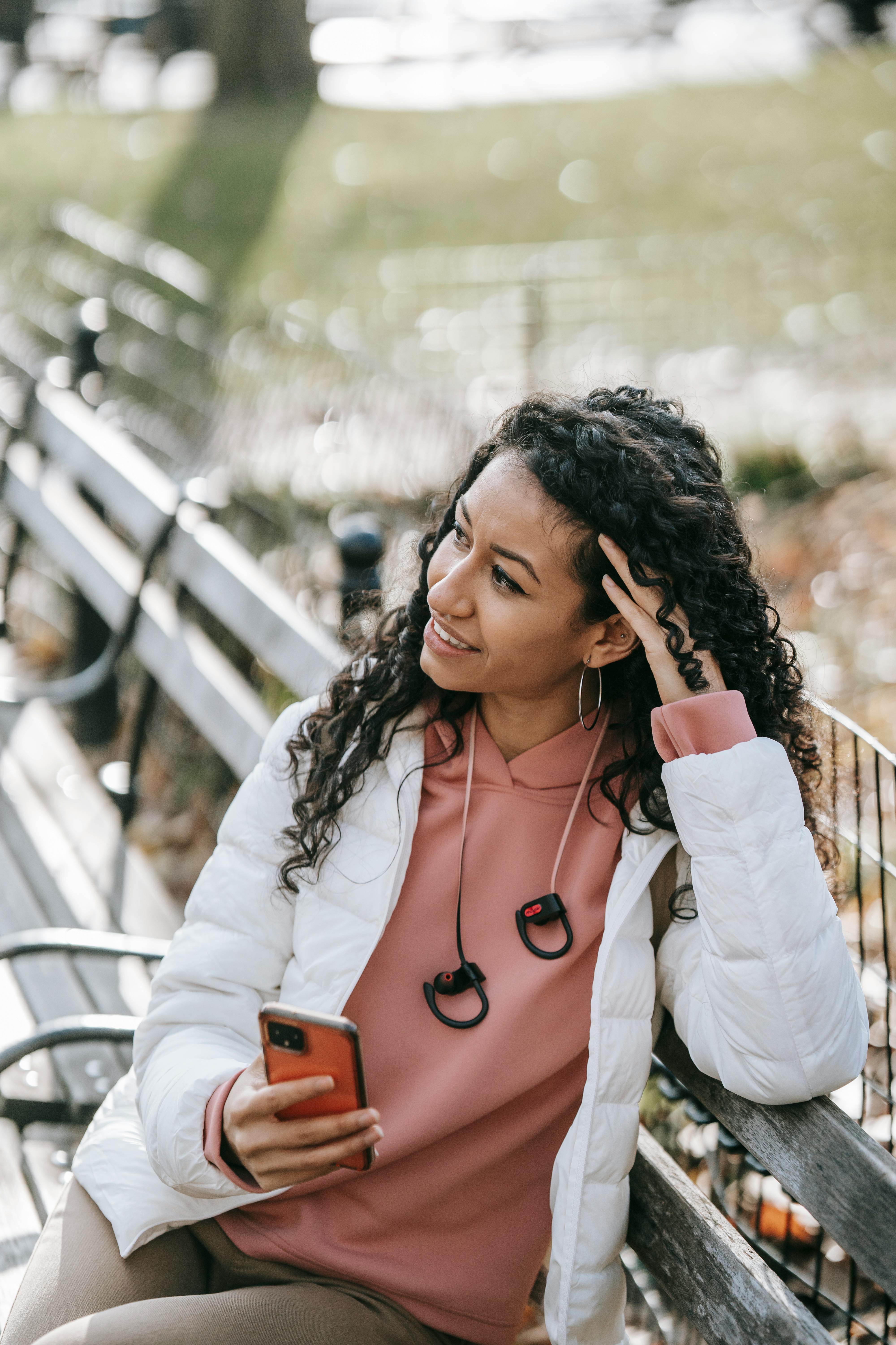 cheerful hispanic woman with smartphone in park