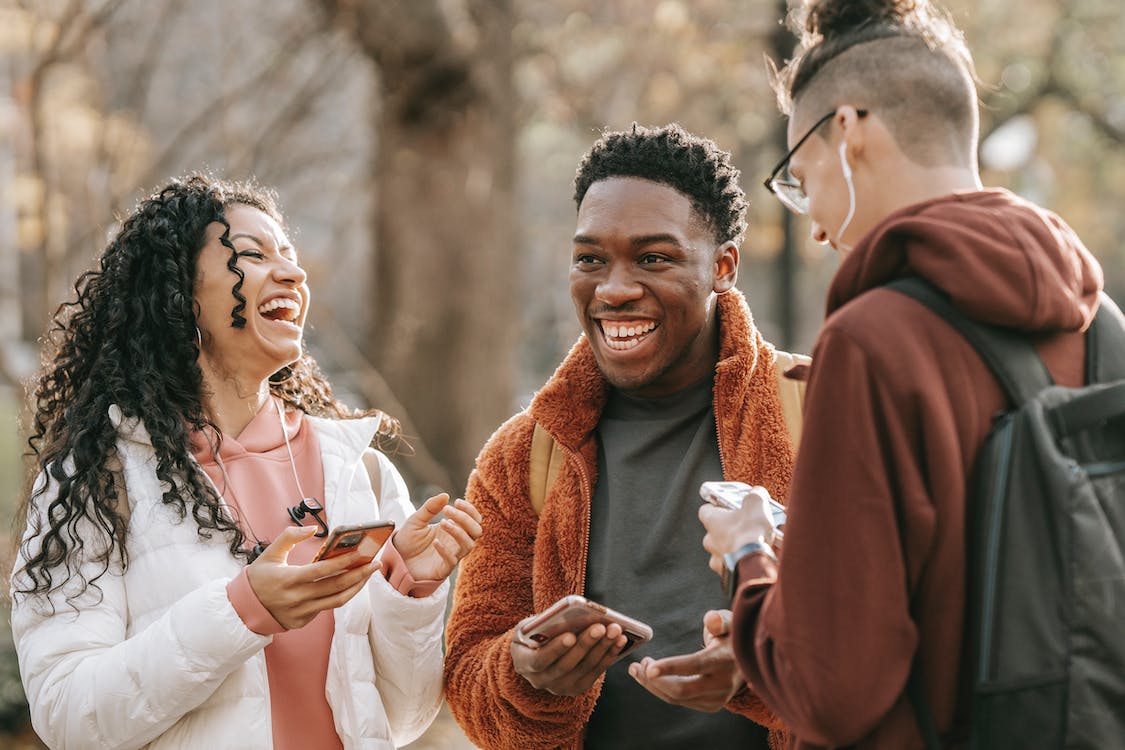 Free Laughing diverse friends with smartphones in park Stock Photo