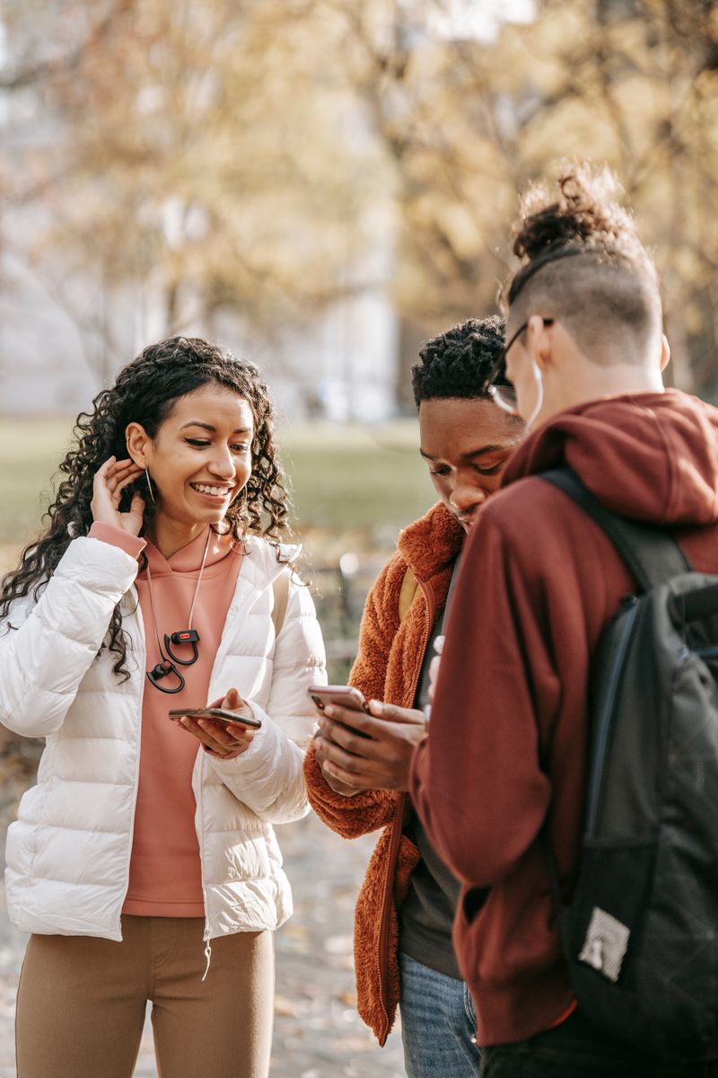 Diverse friends standing outdoors in a park using their smartphones together