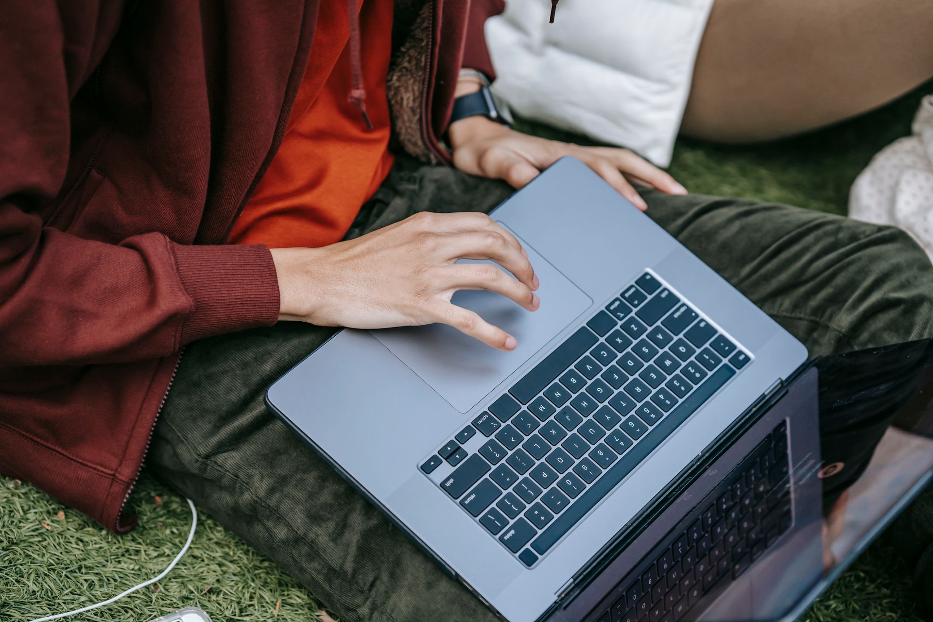 From above of faceless male student surfing internet on modern netbook while sitting on grassy lawn during homework preparation on street