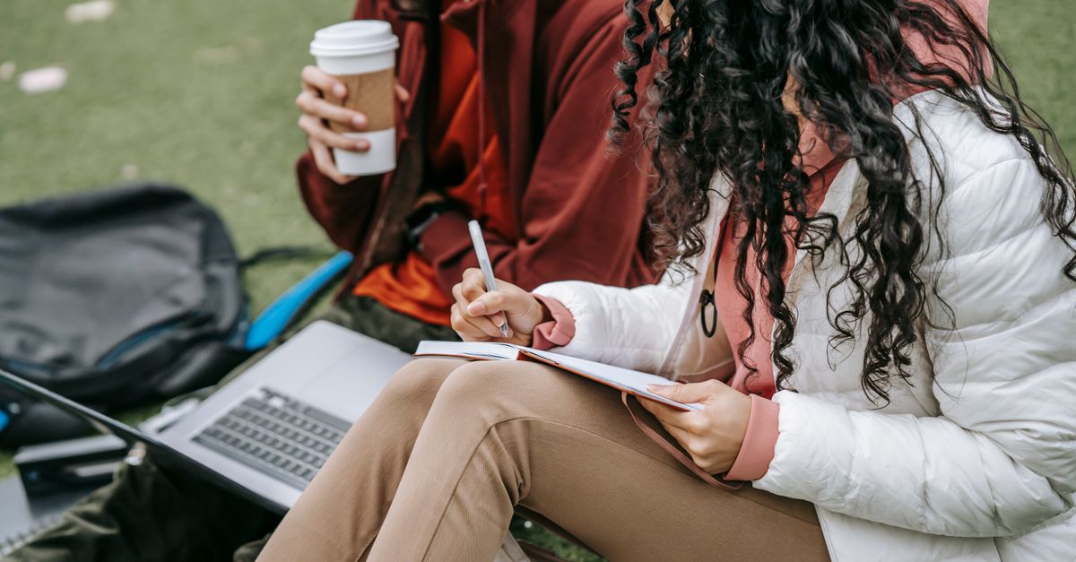 student writing in notebook with coffee and laptop, feeling relaxed