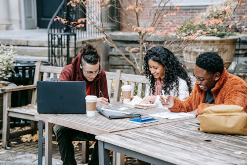 Cheerful multiethnic students studying at table on terrace