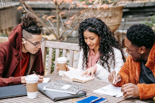 Cheerful multiethnic students with notebooks studying at table