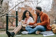Multiethnic couple with notebooks communicating on grassy lawn while studying together