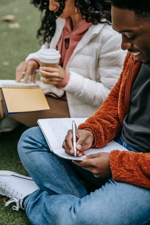 Crop multiracial students writing in notepads on street