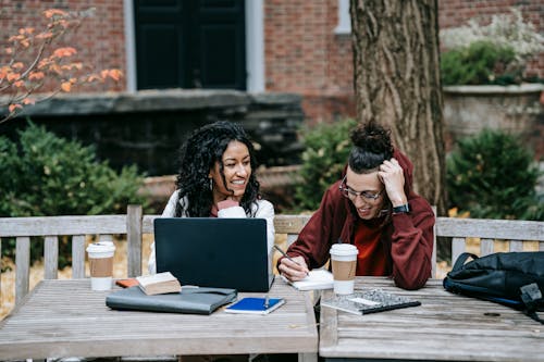 Diverse students working together at table with laptop in park