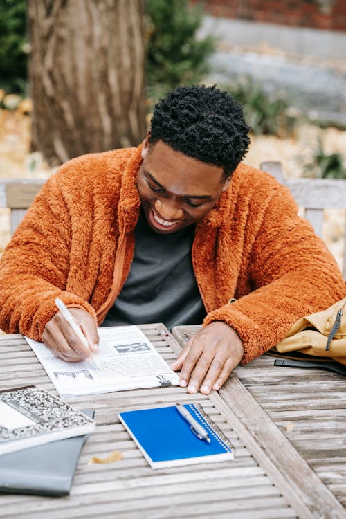 Free From above of cheerful young African American male smiling while studying and examining report on paper at table with planner Stock Photo