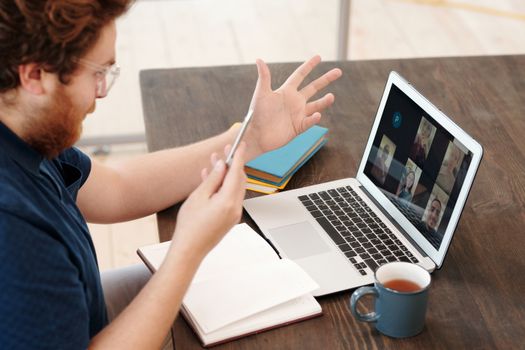 Man engaged in a virtual meeting at home with laptop and tea, chatting and studying online.