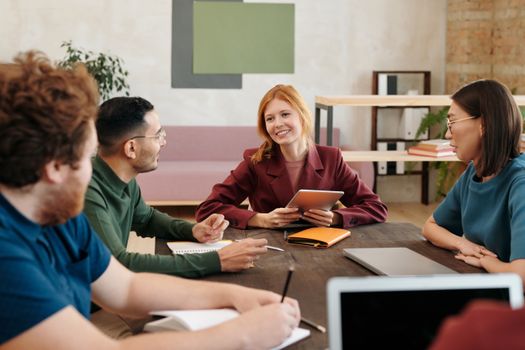 A group of young professionals engaged in a team meeting around a table in a modern office setting.