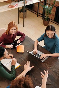 Diverse team discussing project using laptops and tablets at a modern office table.