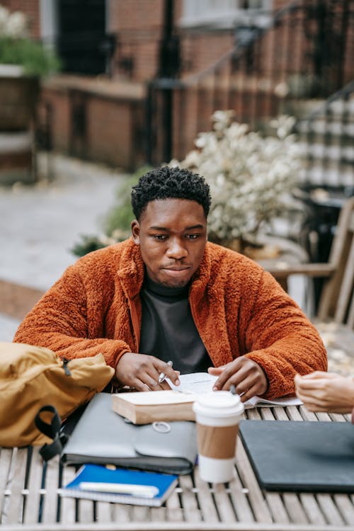 Young black man pondering while studying at table with coffee