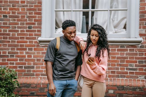 Free Cheerful multiethnic young friends looking at screen of mobile phone near brick building in daytime Stock Photo