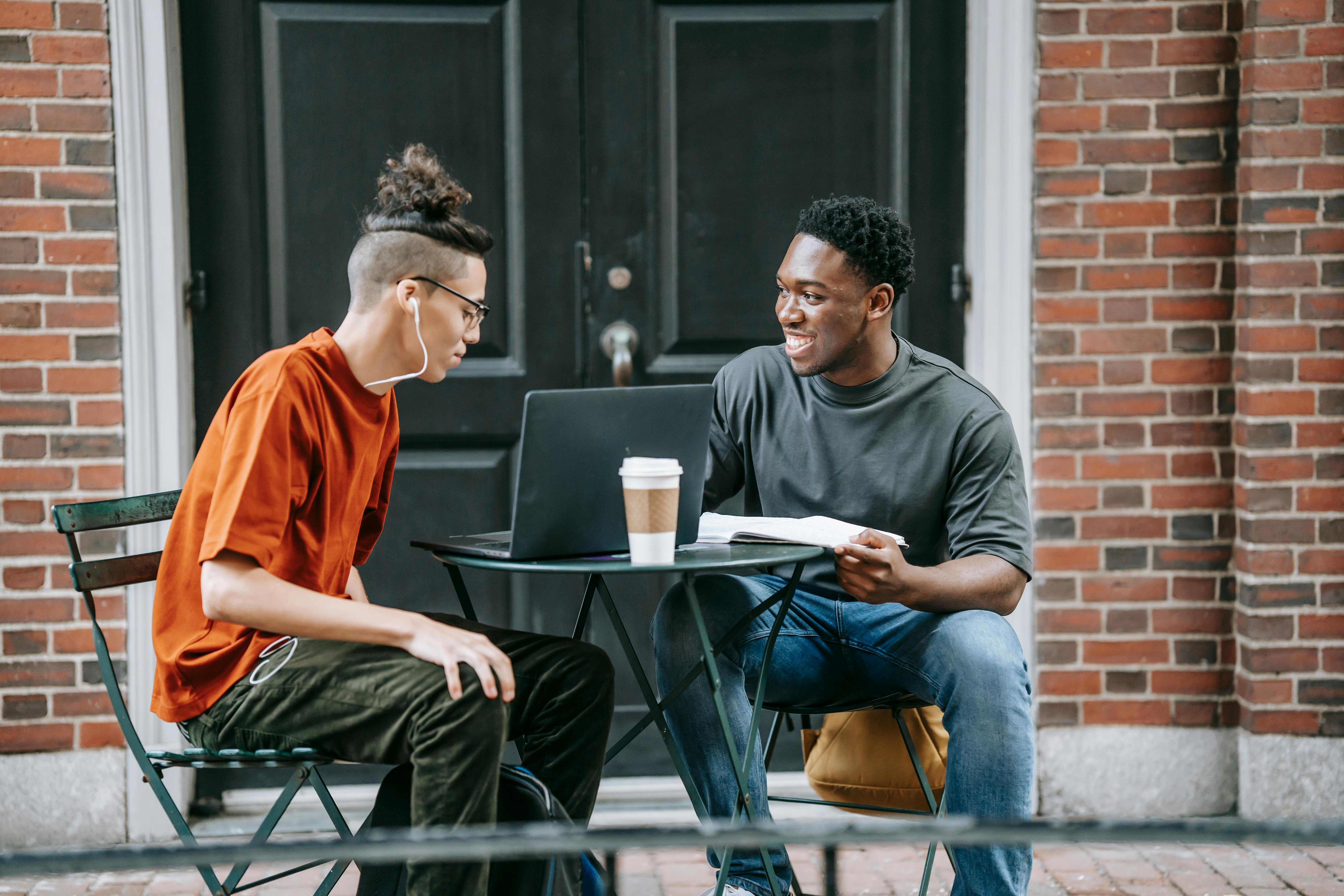 young happy multiethnic students talking at table with laptop