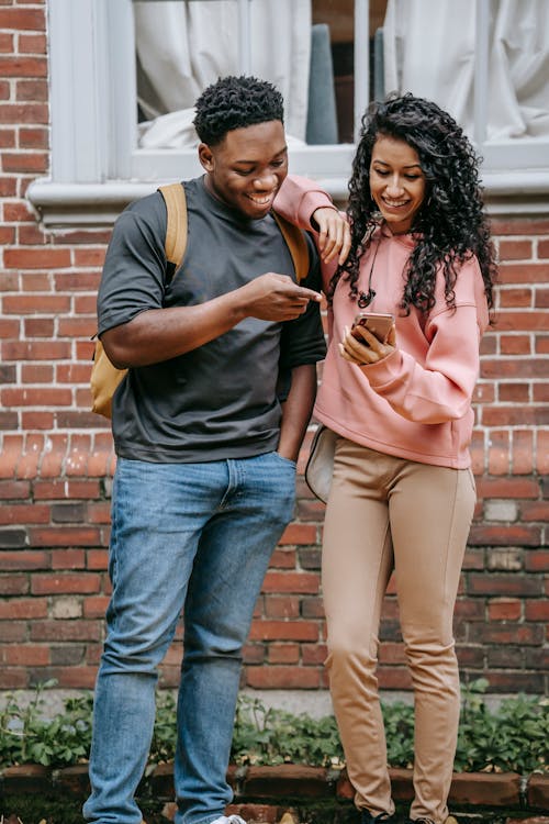 Happy diverse students sharing smartphone together and smiling