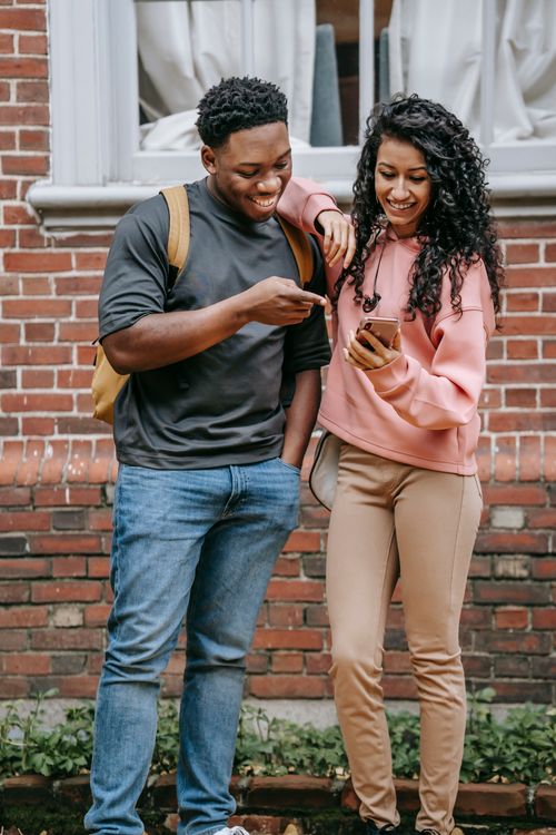 Free Cheerful young multiracial male and female friends in casual clothes smiling while standing together on street and watching funny video on smartphone Stock Photo