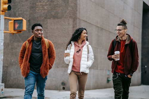 Happy young multiracial friends smiling while walking on street with takeaway coffee