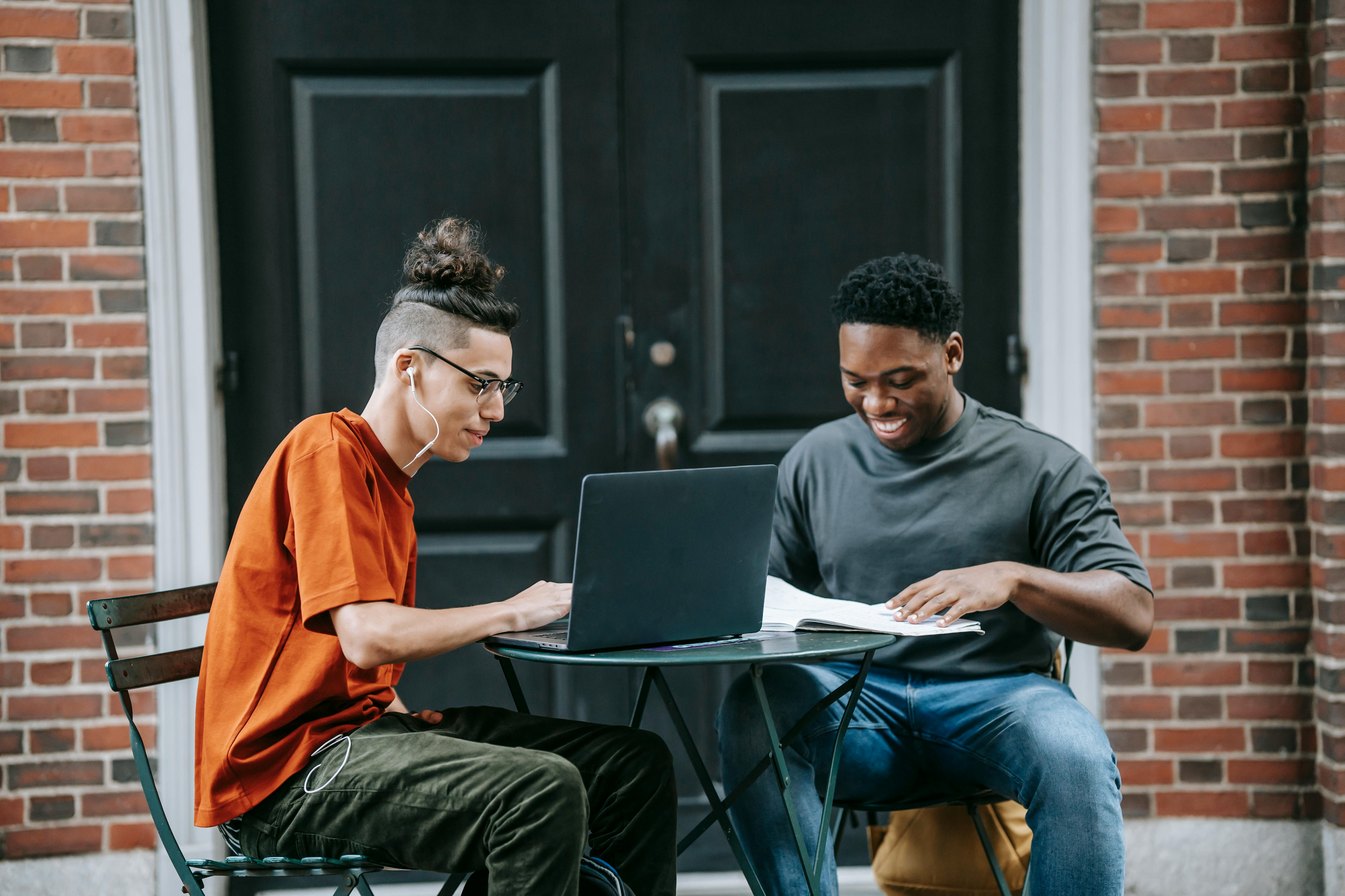 happy young multiracial men working online on laptop in street cafe