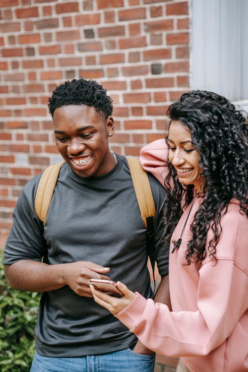 Free Joyful multiethnic teens laughing while sharing smartphone on street Stock Photo