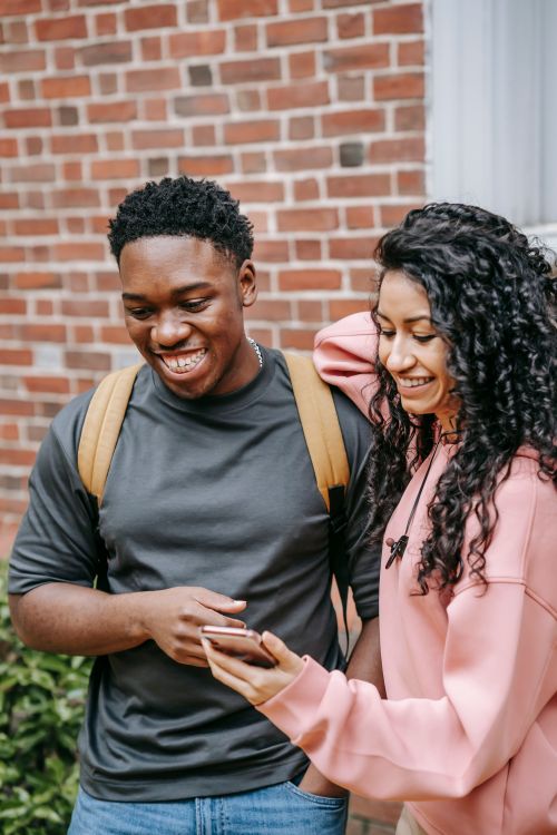 Free Cheerful young diverse male and female best friends in casual clothes laughing while watching funny video on mobile hone after university Stock Photo
