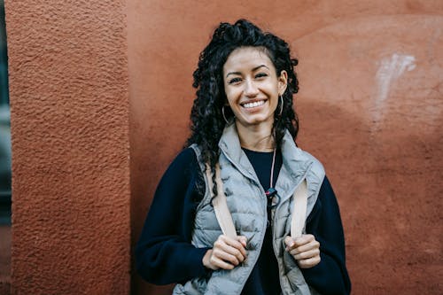 Cheerful young ethnic female standing near shabby stone wall and smiling