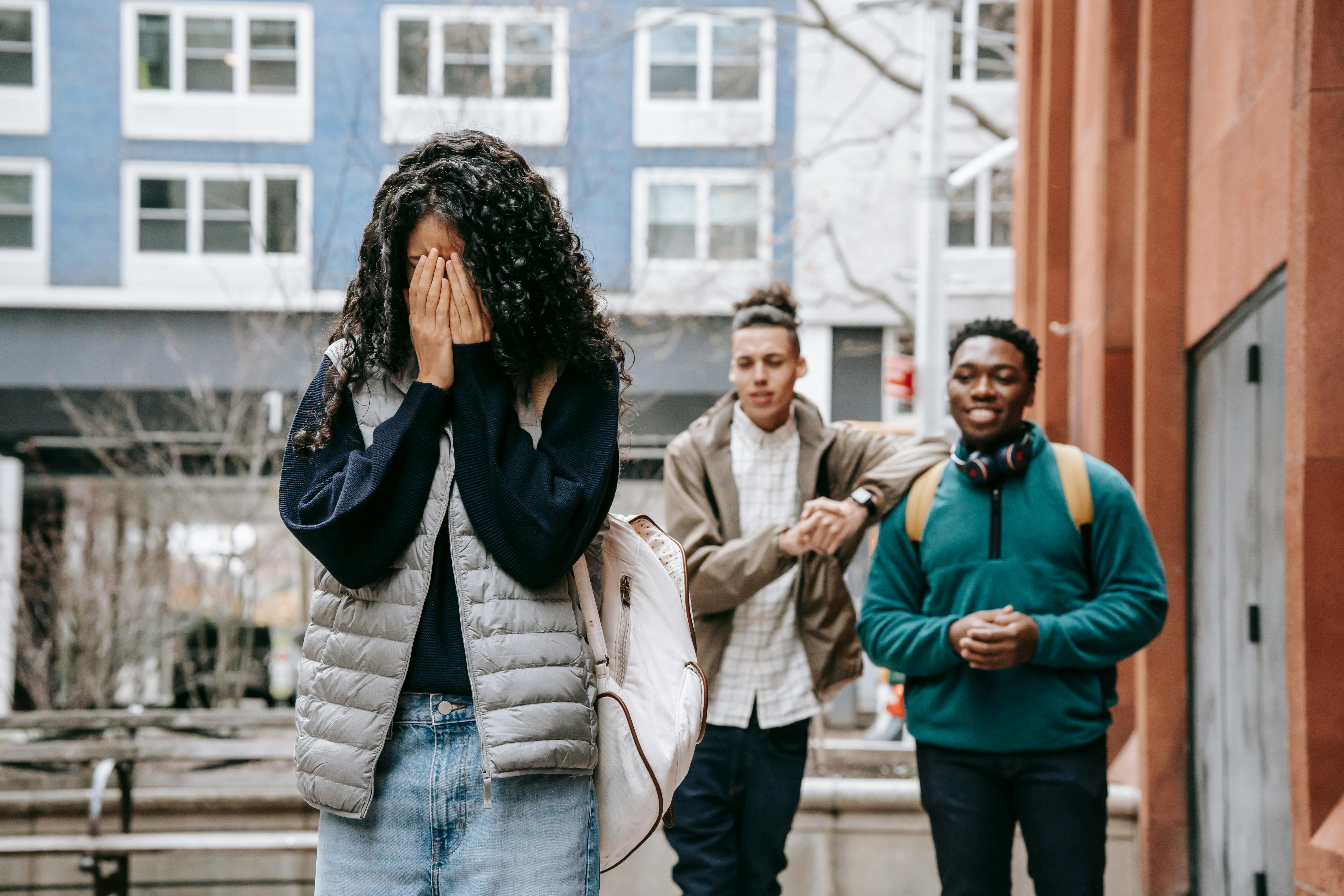 diverse male teenagers bullying anonymous lady covering face with hands