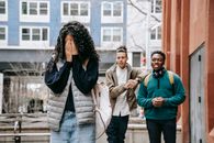Diverse male teenagers bullying anonymous lady covering face with hands