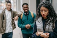 Laughing multiracial teenage boys mocking at depressed young ethnic female standing on street after school