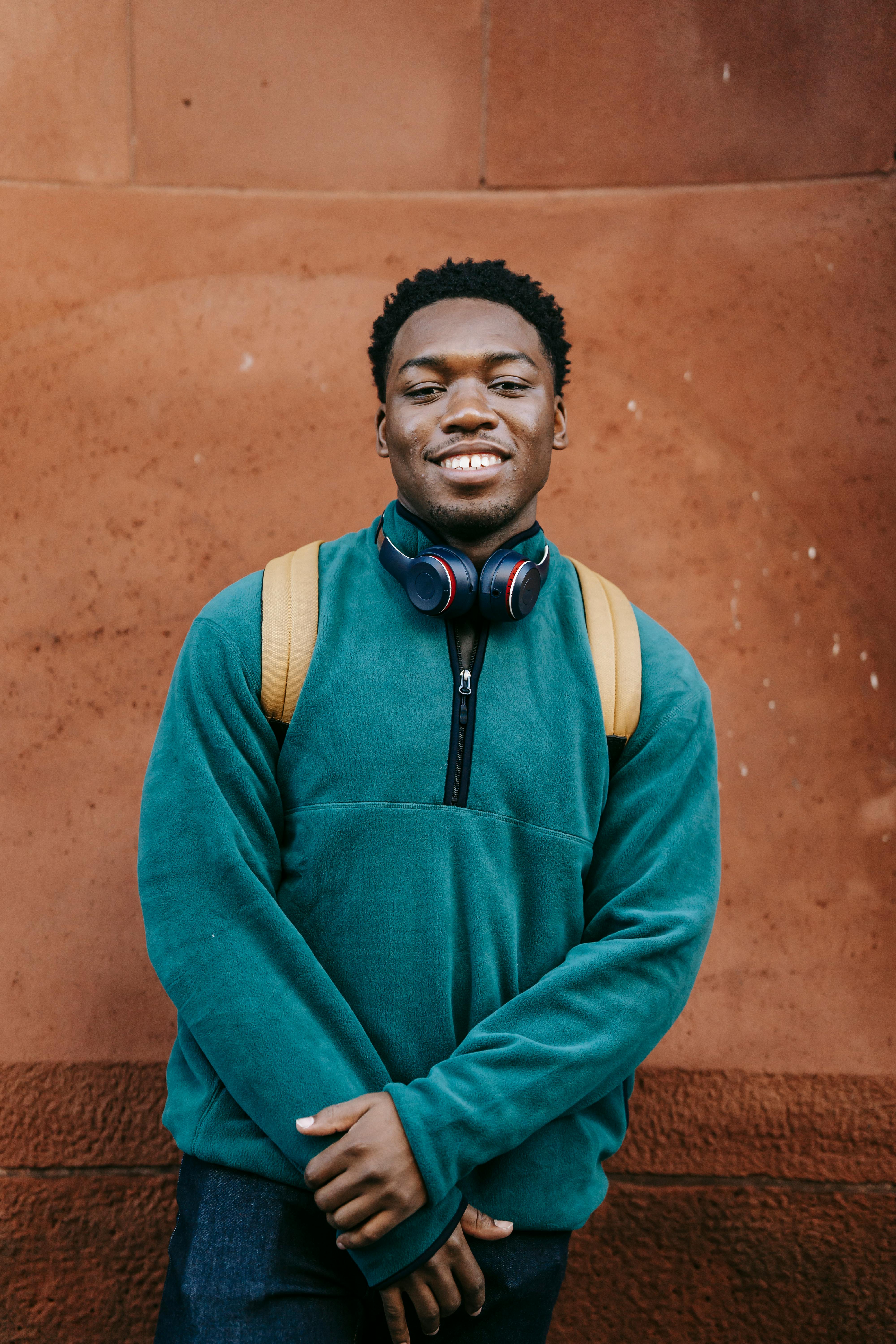 cheerful young ethnic male millennial standing near stone wall and smiling