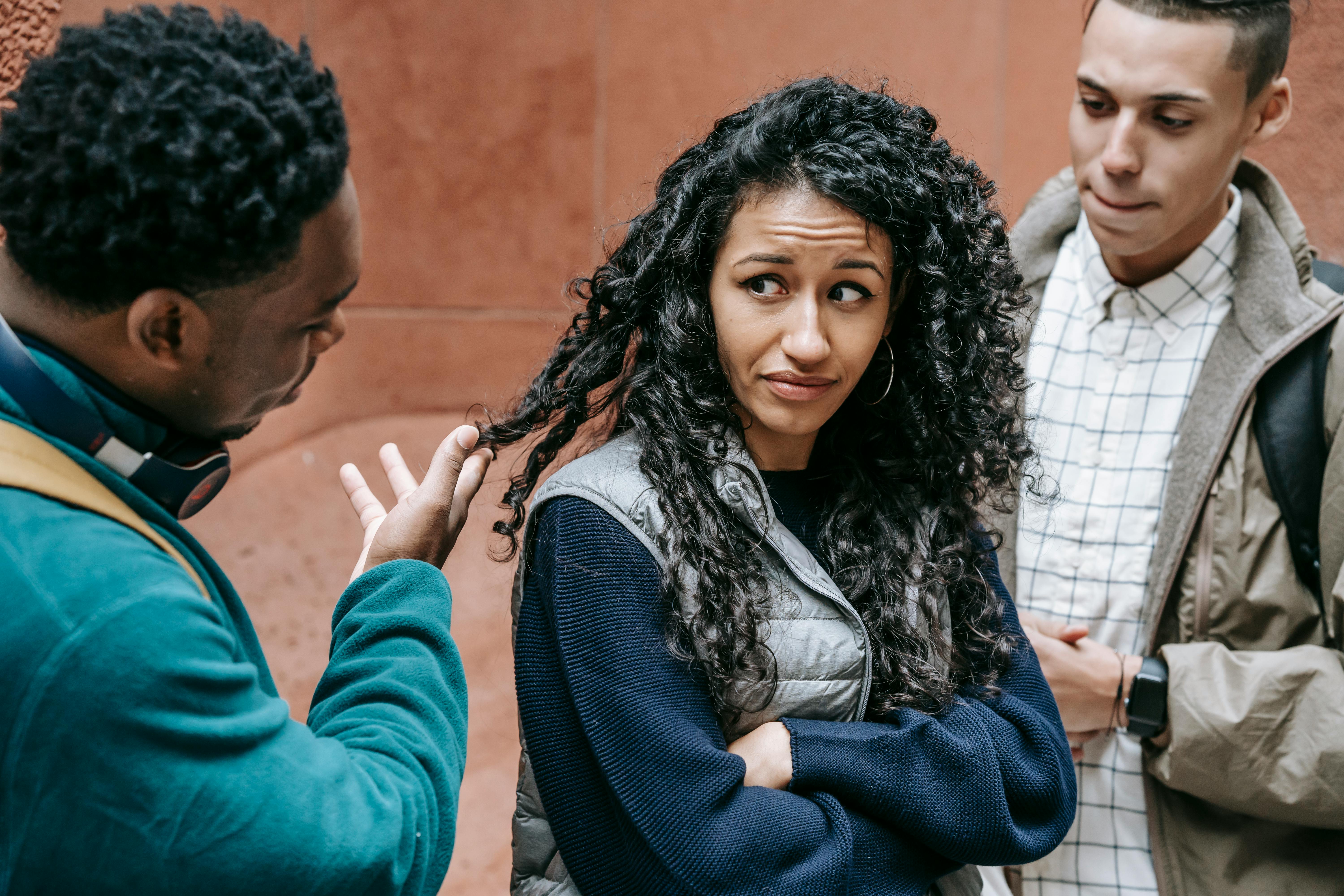 young diverse guys touching hair of upset ethnic female student