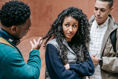 Free Frightened young ethnic female standing on street with crossed arms and looking at African American abusing male groupmate Stock Photo