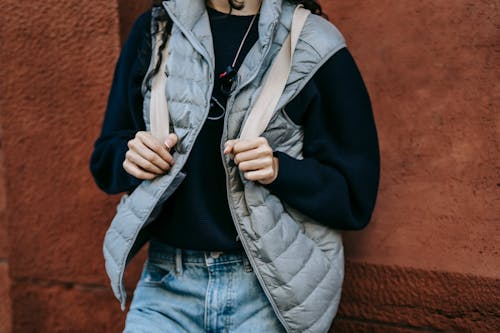 Free Crop unrecognizable female in trendy outfit and backpack leaning on stone wall while resting alone on street Stock Photo
