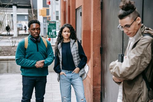 Free Young multiethnic students gossiping about sad male groupmate leaning on wall on street and looking down Stock Photo