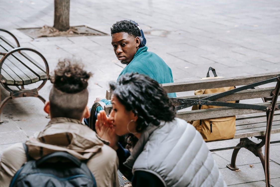 Classmates spreading gossip about African American man on wooden bench 