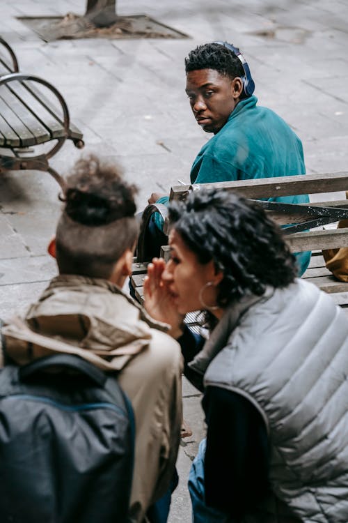 Free Back view of unrecognizable classmates spreading gossip about African American friend on bench Stock Photo