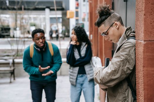 Side view of young student in glasses carrying book while standing in front of multiracial classmates