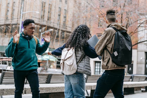 Free Back view of faceless student with backpack pushing away diverse classmates while standing in city park Stock Photo