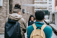 Back view of faceless multiracial friends with backpacks blocking way for Latin American classmate