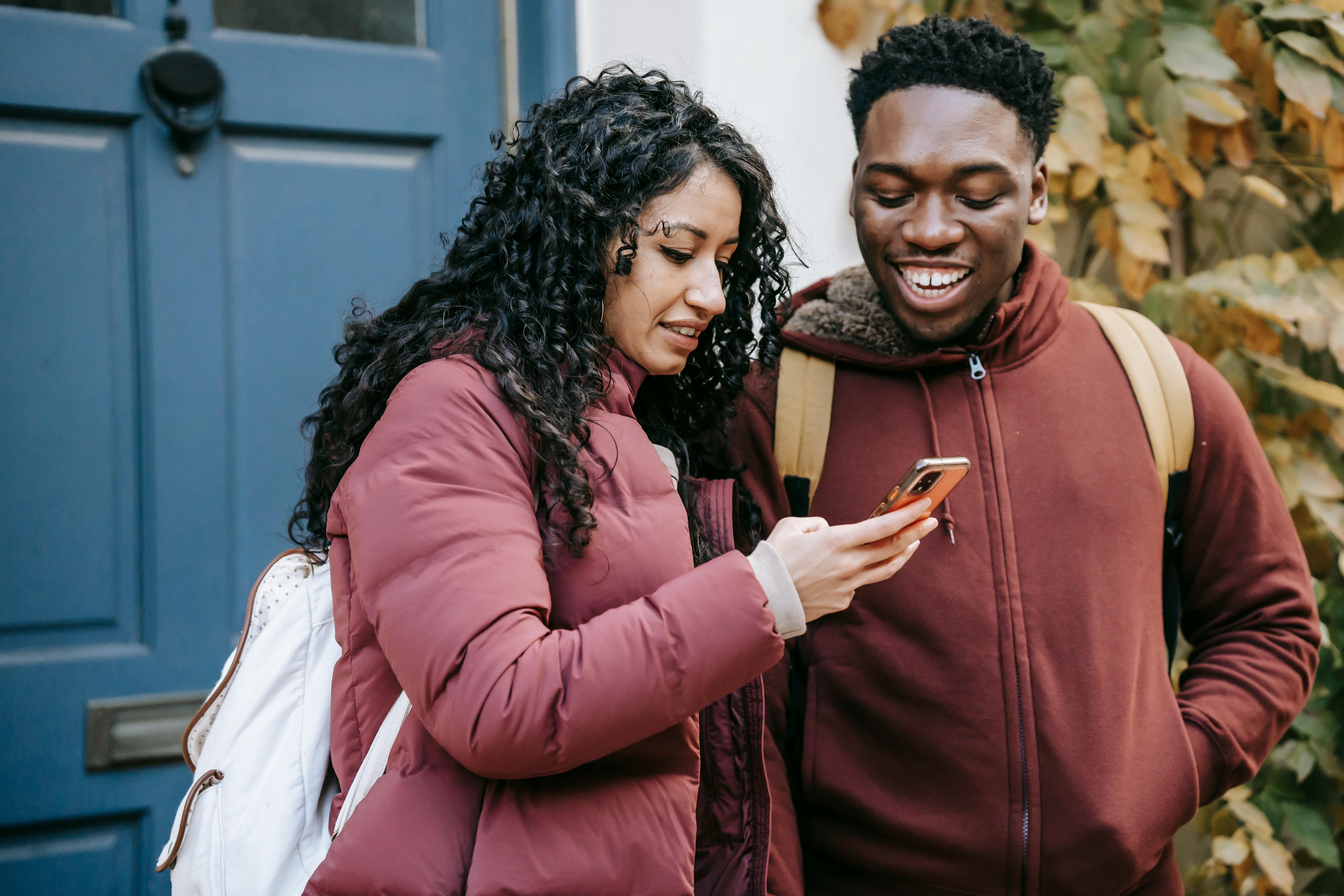 multiethnic happy couple smiling and checking smartphone on street