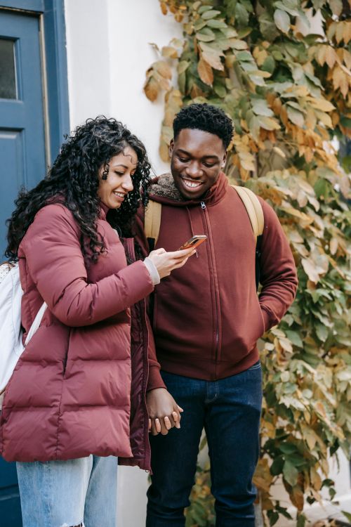 Free Cheerful young multiracial friends using mobile phone on street near urban building in daytime Stock Photo